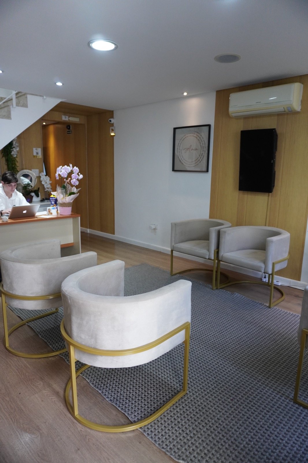 Recepção do Instituto: poltronas de pés dourados, painel de madeira e orquídea sobre o balcão.